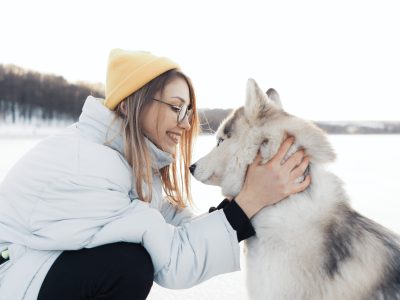 Happy young girl playing with siberian husky dog in winter park. They walk on a frozen lake